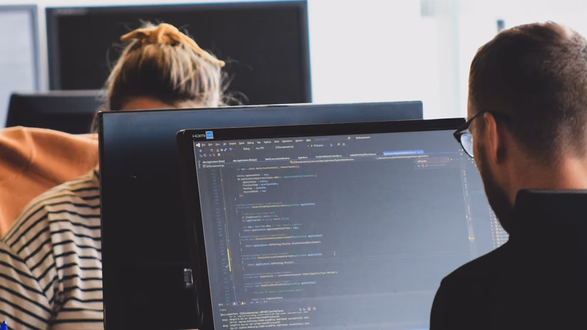 Two people seen from behind, working at computer monitors displaying lines of code